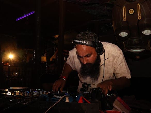 Immortal Baba bent over the mixer in near-darkness, headphones on, a single warm lamp behind him